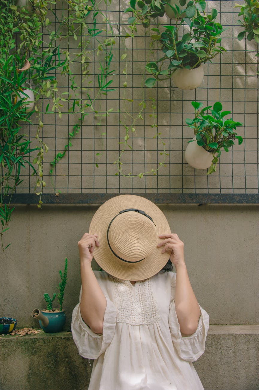 person wearing white elbow sleeved top covering beige sun hat